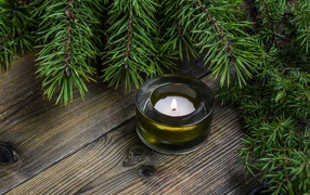 Зажженная свеча на столе с зеленой веткой ели