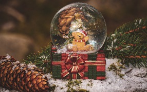 Снежный шар с медвежонком на столе с большой шишкой и еловой веткой 