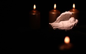 Фигурка ангела освещен горящими свечами на черном фоне