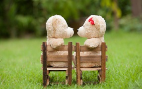 Два плюшевых мишки на деревянных креслах на зеленой траве