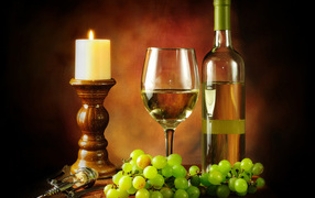 Бутылка белого вина на столе со свечей, белым виноградом и бокалом 