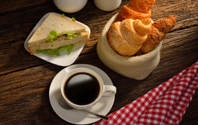 A cup of coffee with croissants and sandwiches for breakfast