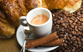 Чашка с горячим кофе на столе с корицей, зернами кофе и выпечкой