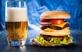 Стакан пива с гамбургером на столе