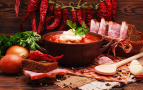A plate of borsch on the table with red hot pepper, garlic, onion, greens and boiled pork