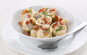Appetizing dumplings with bacon and greens in a white plate
