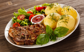 Вареный картофель с куском мяса и салатом на тарелке