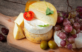 Сыр на разделочной доске с виноградом и оливками