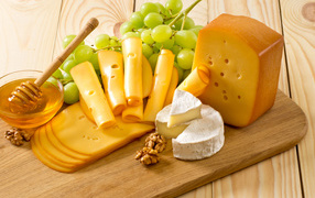 Сыр на столе с белым виноградом, медом и орехами 