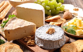 Сыр с плесенью на столе с виноградом, орехами и хлебом