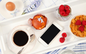 Coffee with cake, cereal and raspberries on the table with a smartphone