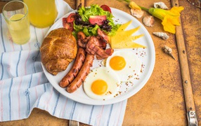 Яичница, салат, сосиски и круассан с соком на завтрак 