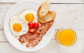 Fried eggs with bacon, croutons and tomatoes on the table with juice