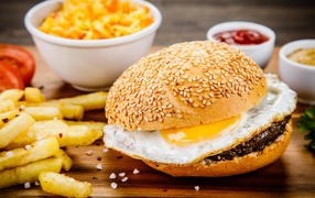 Гамбургер с яичницей на столе с картофелем фри и соусом