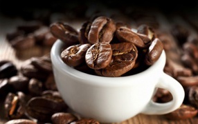 Много кофейных зерен в белой чашке на столе