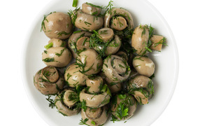 Marinated champignons with greens in a white plate on a white background