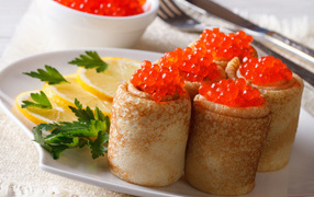 Pancakes with red caviar on a plate with lemons and parsley