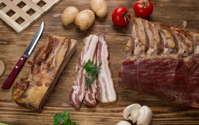 Нарезанное сало на столе с картофелем, помидорами и грибами 