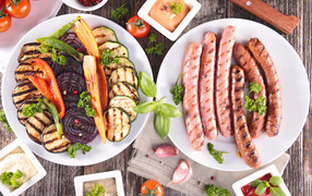 Vegetables and grilled sausages on a table with sauce