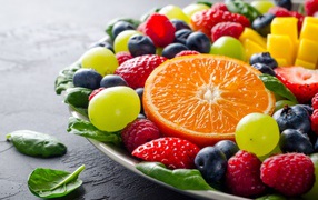 Аппетитные ягоды на тарелке с зелеными листьями базилика