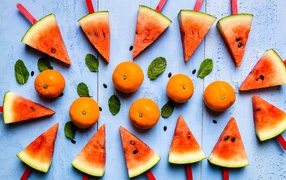 Кусочки арбуза на палочках на столе с мандаринами