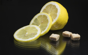 Нарезанный лимон с кусочками коричневого сахара на черном фоне
