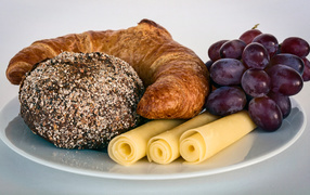 Свежая выпечка с сыром и розовым виноградом на белой тарелке 