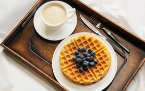 A cup of coffee and sweet waffles with blueberries for breakfast
