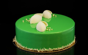 A green glossy cake is reflected in a black surface