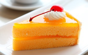 Кусок апельсинового торта с вишенкой на белой тарелке