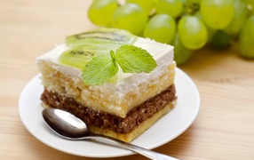 A piece of cake with kiwi and mint on a table with grapes