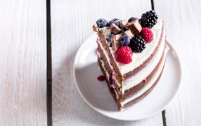 Кусок торта с ягодами малины и черники на блюдце