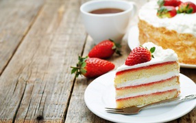 Кусок торта с клубникой на столе с чашкой чая 