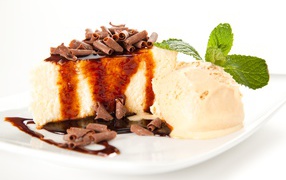 A piece of cheesecake with chocolate and an ice cream ball on a white plate