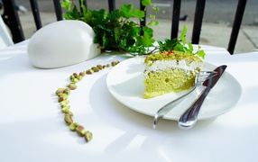 Кусок фисташкового торта на тарелке с вилкой и ножом