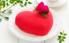 Beautiful cake in the shape of heart on a white dish with a red flower
