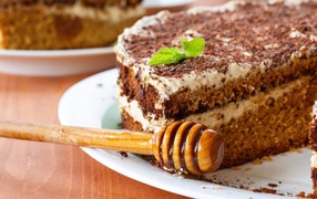 Cake with cream and chocolate on a plate with a spoon for honey