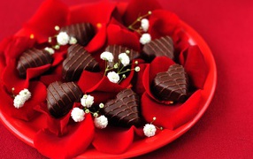 Шоколадные конфеты в форме сердца на тарелке с лепестками розы