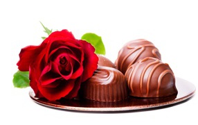 Шоколадные конфеты на тарелке с красной розой на белом фоне