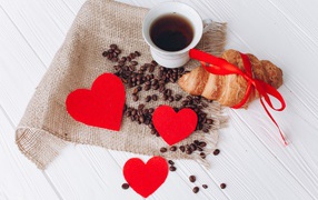Croissant with a cup of coffee and coffee beans on a table with red hearts