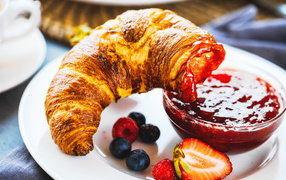 Круассан с джемом и ягодами на тарелке