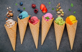 Шарики фруктового мороженого в вафельных рожках на сером фоне