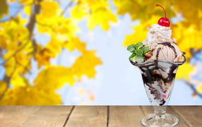 Ice cream sundae with a cherry on the background of yellow leaves