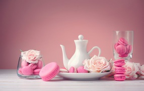 Розовый десерт макарун на столе с белый чайником и цветами розы