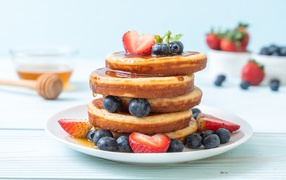Ruddy pancakes with honey, blueberries and strawberries