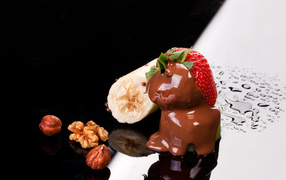Клубника в шоколаде, банан и орехи на черной поверхности