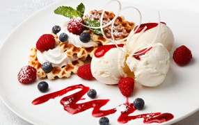 Сладкие вафли с ягодами черники и малины на белой тарелки с шариками мороженого