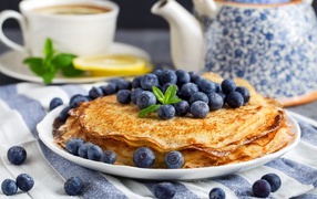 Thin pancakes with blueberries on a table with tea