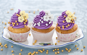 Три вкусных кекса с фиолетовым кремом украшен цветами