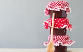 Три баночки варенья с деревянной ложкой на сером фоне